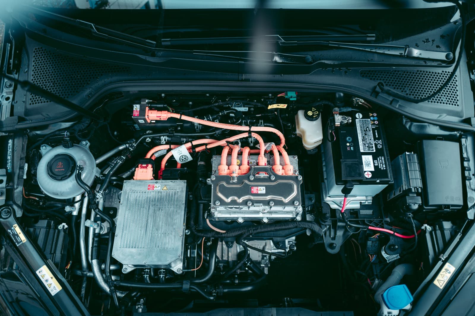 Geöffneter Motorraum eines Hybridfahrzeugs mit orangefarbenen Hochvoltleitungen